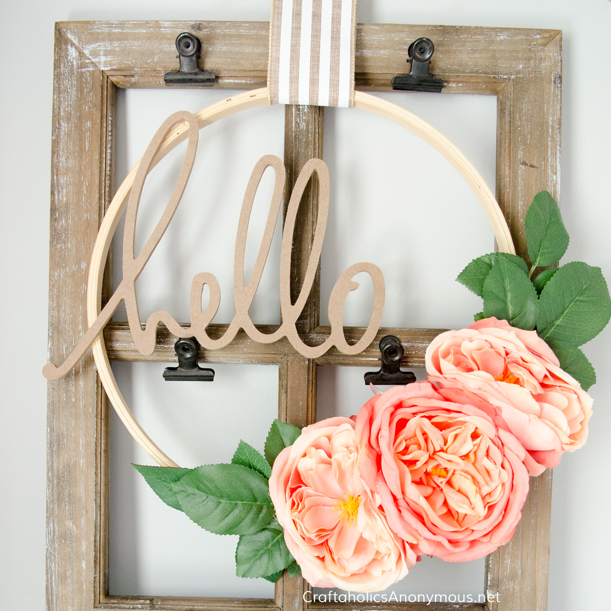 Wood embroidery hoop wreath with three large coral peonies, green leaves and a cut wood hello word on striped ribbon
